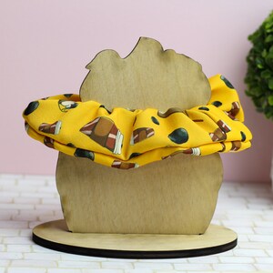 Op de afbeelding: Een houten haarbandhouder in de vorm van een hoofd met een gele haarband met bruine en zwarte ontwerpen.