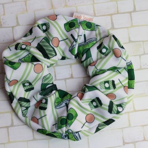 Op de afbeelding: Een groene en witte haarband met een ontwerp van groene drankjes en witte strepen. De haarband heeft een klein label met de tekst "Katie Designs".