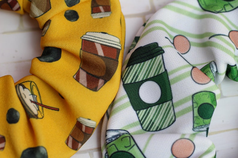 Op de afbeelding: Twee stoffen haarbandjes met een koffiekopjespatroon. Een haarbandje is geel met bruine koffiekopjes en de andere is wit met groene koffiekopjes.