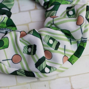 Op de afbeelding: Een witte scrunchie met een groen-wit gestreept patroon. De scrunchie heeft een herhalend patroon van groene koffiebekers en groen-wit gestreepte lolly's.