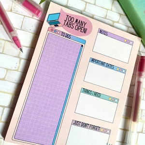 Op de afbeelding: Een roze en blauwe notitieblok met een computerschermdesign en de tekst "Too Many Tabs Open!" Het notitieblok heeft secties voor to-do's, notities, belangrijke data, dingen die ik nodig heb en dingen die ik niet mag vergeten.