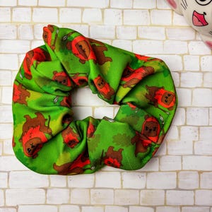 Peut inclure: Un chouchou vert avec un motif répété d'ours bruns portant des capes rouges à capuchon.