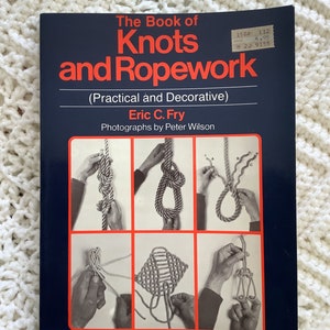 May include: A vintage book titled "The Book of Knots and Ropework" with a navy blue cover and orange lettering. The cover features illustrations of various knots. The book is by Eric C. Fry, with photographs by Peter Wilson.