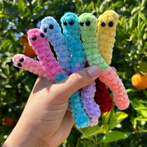 May include: A set of seven colorful crocheted worm toys. The worms are in a rainbow color pattern, starting with red, pink, light blue, green, yellow, and ending with a light purple worm.