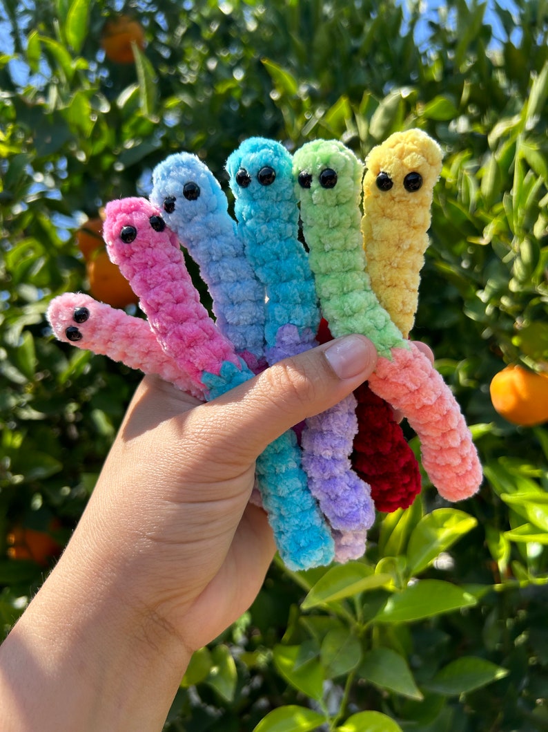 May include: A set of seven colorful crocheted worm toys. The worms are in a rainbow color pattern, starting with red, pink, light blue, green, yellow, and ending with a light purple worm.