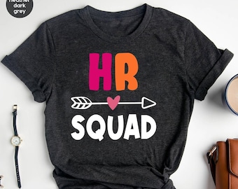 May include: Heather dark grey t-shirt with a white arrow and heart graphic. The text "HR SQUAD" is printed in white below the arrow. The words "HR" are printed in pink and orange above the arrow.