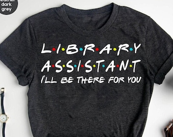 Puede incluir: Camiseta gris oscuro jaspeada con el texto "LIBRARY ASSISTANT I'LL BE THERE FOR YOU" en blanco con puntos de colores entre cada letra.