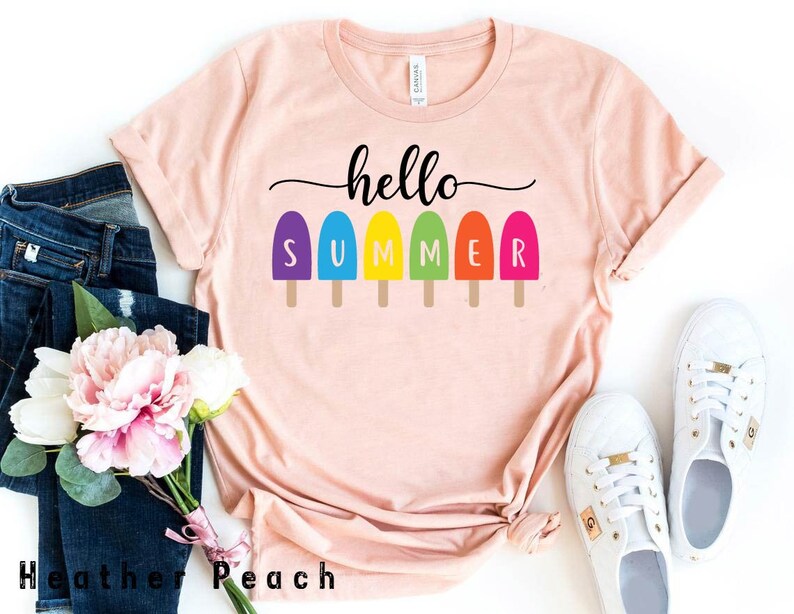 May include: A light peach-colored t-shirt with the words "hello SUMMER" in black and colorful popsicle graphics. The shirt is styled with blue jeans, white sneakers, and a bouquet of pink and white flowers.