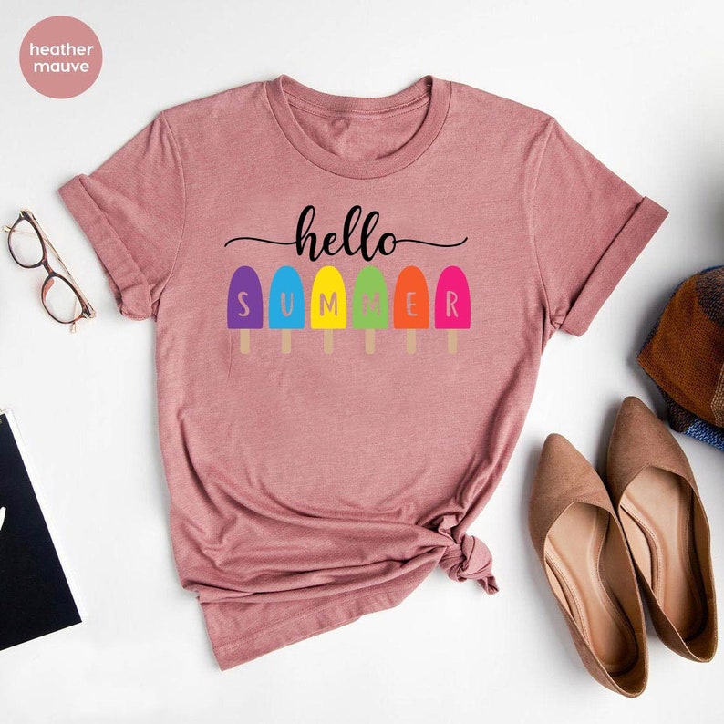 May include: Heather mauve t-shirt with the words "hello SUMMER" and colorful popsicle graphics. The shirt has a crew neck and short sleeves. The text and graphics are in black, purple, blue, yellow, green, orange, and pink.