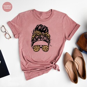 May include: Heather mauve t-shirt featuring a graphic of a woman with a messy bun, leopard print headband, and leopard print sunglasses.