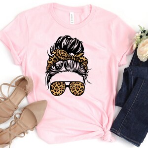 May include: Pink t-shirt featuring a graphic of a woman with a messy bun, leopard print headband, and leopard print sunglasses.