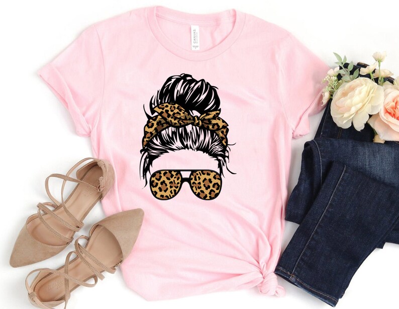 May include: Pink t-shirt featuring a graphic of a woman with a messy bun, leopard print headband, and leopard print sunglasses.