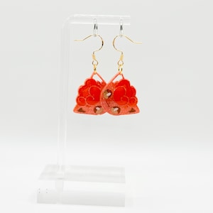 Puede incluir: Un par de pendientes colgantes con un diseño floral rojo y naranja. Los pendientes están hechos de resina y tienen ganchos dorados.