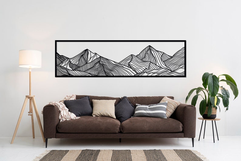 Puede incluir: Decoraci&oacute;n de pared de arte de l&iacute;nea en blanco y negro que representa una cordillera. La obra de arte est&aacute; enmarcada en un marco negro y est&aacute; colgada en una pared blanca sobre un sof&aacute; marr&oacute;n.