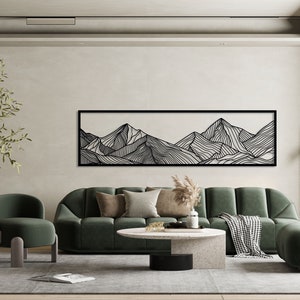 Puede incluir: Un dise&ntilde;o de interior de sala de estar con un sof&aacute; seccional de terciopelo verde, un sill&oacute;n de terciopelo verde, una mesa de caf&eacute; y una impresi&oacute;n de arte de l&iacute;nea en blanco y negro de monta&ntilde;as en la pared.