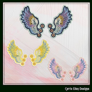 May include: Four pairs of embroidered wings in different colors. The wings are in shades of blue, yellow, and pink. The wings are on a white background with a pink and white textured surface. The text "Carrie Ellen Designs" is at the bottom of the image.