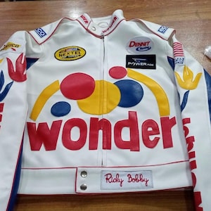Peut inclure: Une veste de course blanche arborant le mot Wonder en grandes lettres rouges sur la poitrine, agrémentée de patchs circulaires jaunes, rouges et bleus. Les manches présentent des motifs floraux bleus et rouges, avec divers logos et le nom Ricky Bobby.