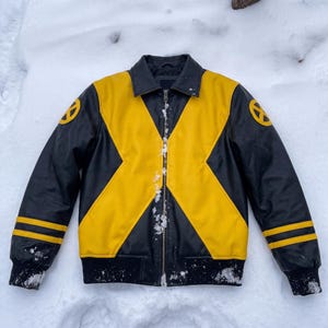 May include: A black and yellow jacket featuring a large X-shaped pattern across the front, a central zipper, a collar, and circular X-Men logos on both shoulders. The sleeves have two horizontal yellow stripes near the black ribbed cuffs.