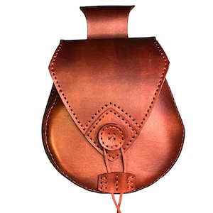 May include: A brown leather pouch with a flap closure and a button detail. The pouch has a rounded bottom and a strap for carrying. The leather has a rich, warm tone, and the stitching is visible. The pouch is likely designed for carrying small items.