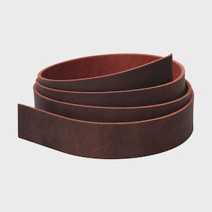 May include: A long, continuous strip of dark brown leather coiled into a circular shape. The leather features a smooth, matte exterior surface with a visible grain and a contrasting reddish-brown interior side, showing the natural texture of the material.