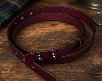 May include: A thin, deep burgundy leather belt featuring a smooth exterior finish and a textured interior. The belt is secured with two dark metallic stud fasteners and includes a series of evenly spaced adjustment holes along the strap length.