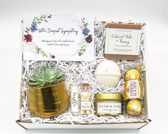 May include: A sympathy gift box with a succulent in a gold pot, a card with floral accents and the text "With Deepest Sympathy", a bar of soap, bath bomb, candle, lip balm, matches, and chocolates.