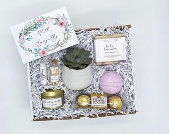 May include: A gift box filled with a succulent in a white pot, a bar of lavender soap, a bath bomb, a candle, lip balm, matches, and chocolates. A card with the words "With Sympathy" is also included. The box is filled with white paper filler.