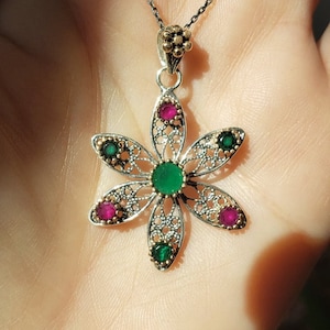 May include: A silver filigree flower pendant necklace with green and pink gemstones. The pendant is on a silver chain.