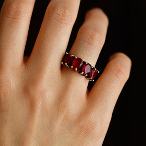 May include: A gold ring with a row of six red oval-shaped gemstones.