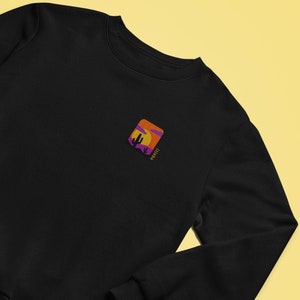 May include: Black sweatshirt with a small embroidered image of a desert sunset with a cactus and the word "wander" in purple text.