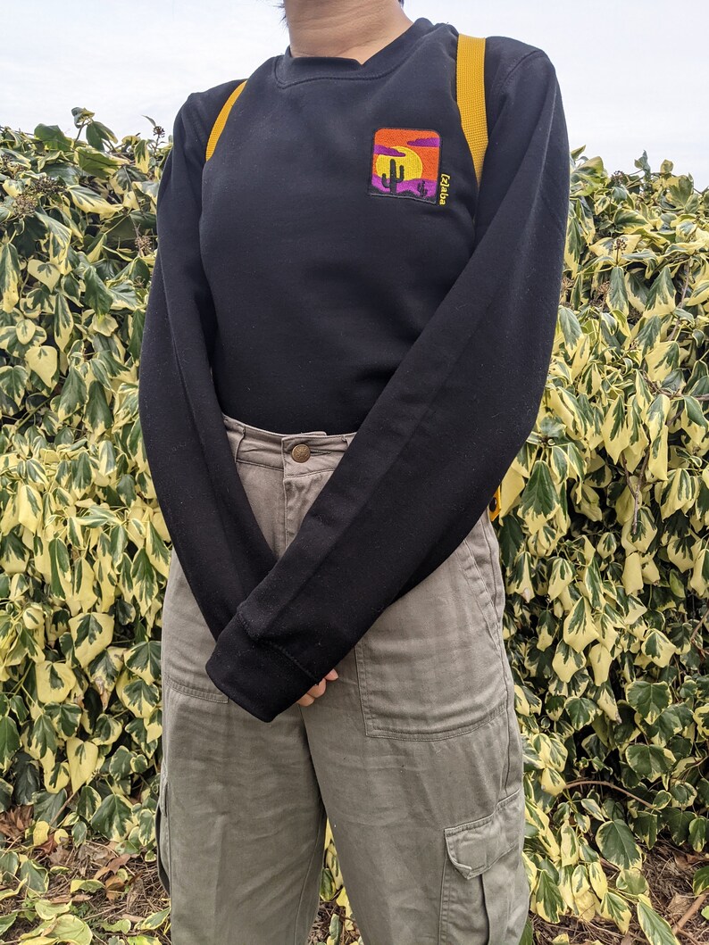 May include: Black long-sleeve sweatshirt with a colorful embroidered patch of a sunset and cactus with the text "Arizona" on it.