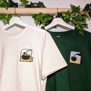 Puede incluir: Dos camisetas con dise&ntilde;os bordados. La camiseta blanca tiene un cuenco de fideos ramen con palillos. La camiseta verde tiene un cuenco de t&eacute; verde con una taza de t&eacute;. Ambos dise&ntilde;os tienen la palabra "Izakaya" escrita en ellos.
