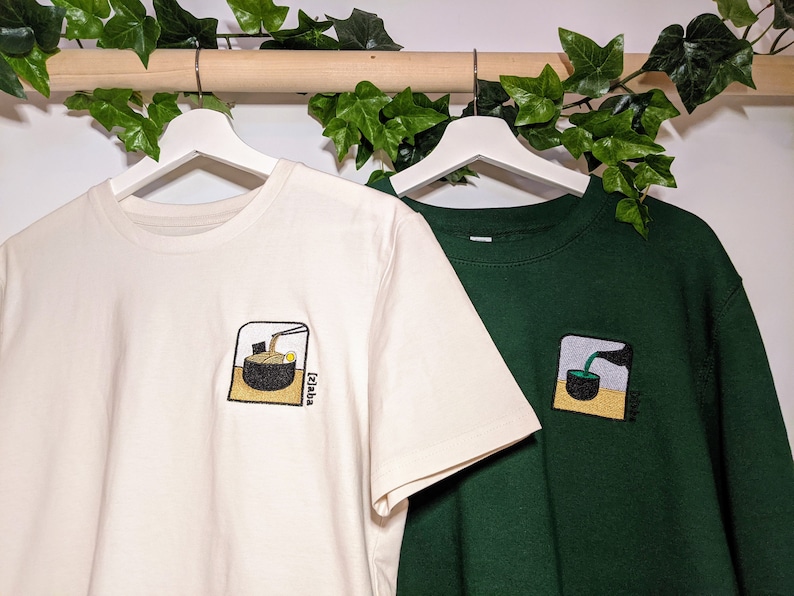 Puede incluir: Dos camisetas con dise&ntilde;os bordados. La camiseta blanca tiene un cuenco de fideos ramen con palillos. La camiseta verde tiene un cuenco de t&eacute; verde con una taza de t&eacute;. Ambos dise&ntilde;os tienen la palabra "Izakaya" escrita en ellos.