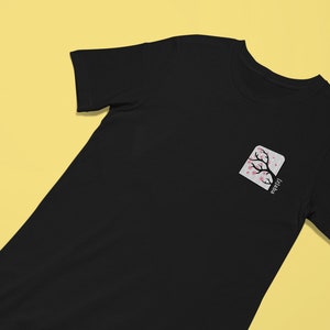 May include: Black t-shirt with a white square pocket featuring a pink cherry blossom tree and the word "Japan" written vertically.