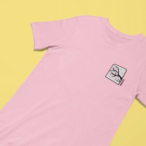 May include: A pink t-shirt with a black and pink cherry blossom tree graphic in a square frame with the text "Jizai-kan" below the image.