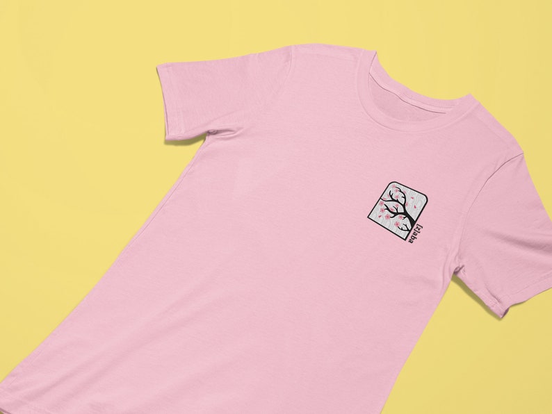 May include: A pink t-shirt with a black and pink cherry blossom tree graphic in a square frame with the text "Jizai-kan" below the image.