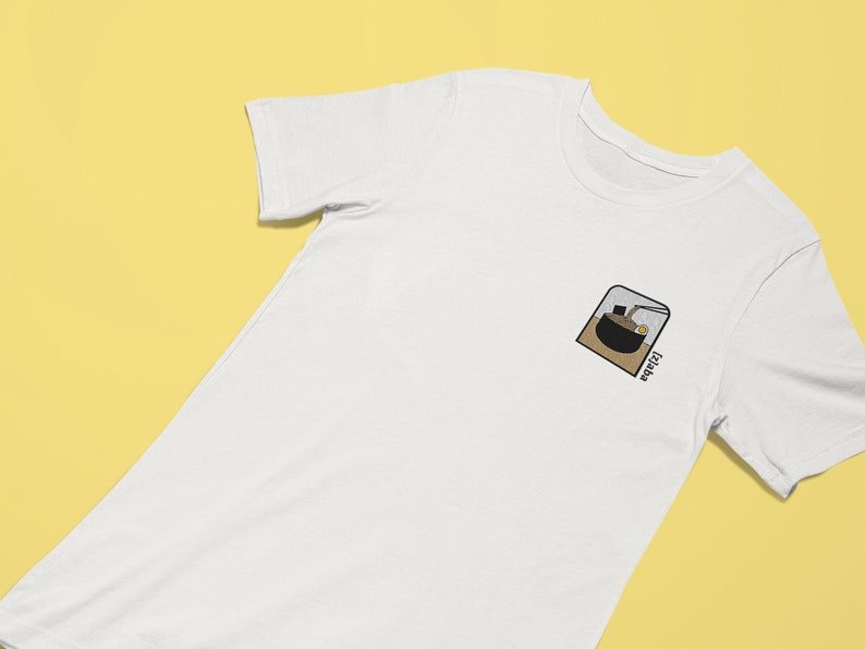 Puede incluir: Camiseta blanca con una peque&ntilde;a imagen bordada de un cuenco de fideos ramen con la palabra "Ramen" escrita debajo.