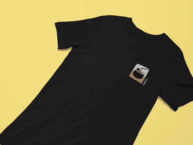 Puede incluir: Camiseta negra con una imagen bordada en blanco de un cuenco de ramen y el texto "Ramen" en la parte delantera.
