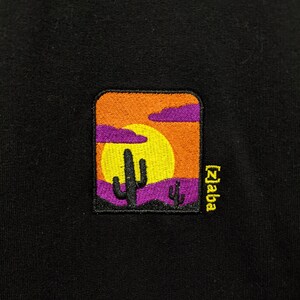 May include: Black t-shirt with an embroidered patch of a sunset scene with a cactus and the text "[z]aba" in yellow.