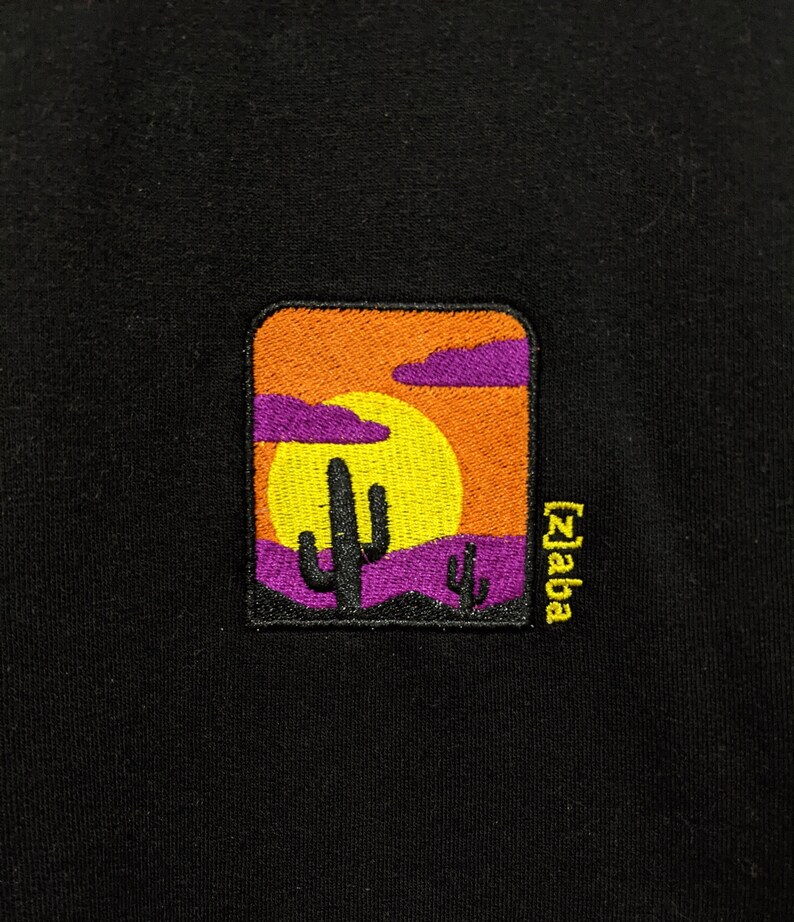 May include: Black t-shirt with an embroidered patch of a sunset scene with a cactus and the text "[z]aba" in yellow.