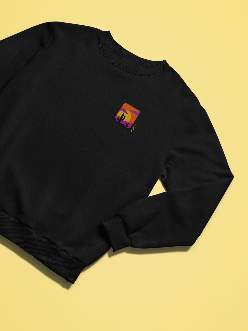 May include: Black sweatshirt with a small embroidered image of a desert sunset with a cactus and the word "wander" in purple text.