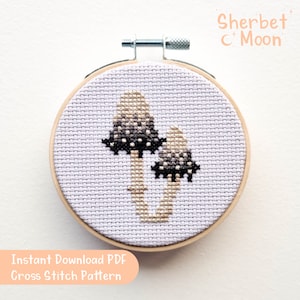 May include: A cross stitch pattern of two mushrooms with black and white spots on a light purple background. The pattern is framed in a wooden hoop. The text "Sherbet C Moon" is written in the top right corner of the image. The text "Instant Download PDF Cross Stitch Pattern" is written in the bottom left corner of the image.