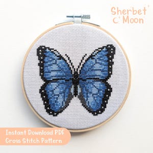 May include: A cross-stitch pattern of a blue butterfly with black detailing, displayed in a wooden embroidery hoop. The text "Instant Download PDF Cross Stitch Pattern" is visible. The shop name "Sherbet C Moon" is also visible.