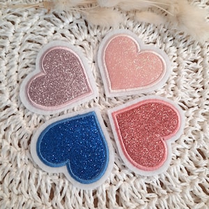Könnte beinhalten: Vier Filz-Herzen mit Glitzer. Die Herzen sind rosa, hellrosa, blau und koralle.