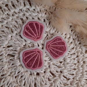 Könnte beinhalten: Drei rosa Glitzer-Muschel-Patches mit weißem Filzrücken.