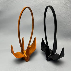 Può includere: Due supporti per cuffie in pelle, uno arancione e uno nero. Ogni supporto ha una parte superiore curva e una base stilizzata. Questi supporti sono progettati per contenere le cuffie.