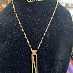 May include: A gold chain necklace with a pendant featuring a geometric design with a small diamond at the top.