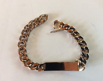 May include: A silver chain bracelet with a blank rectangular tag. The chain is a curb style.