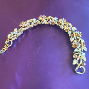 Könnte beinhalten: Ein goldfarbenes Armband mit einem Rankendesign und schimmernden orangefarbenen und klaren Strasssteinen.