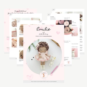 May include: A crochet amigurumi pattern for a doll named Emilie and a bunny. The pattern is printed on pink paper with hearts and includes instructions for making the doll and bunny. The doll has brown curly hair, a pink dress, and white shoes. The bunny is white with pink ears and a pink nose.